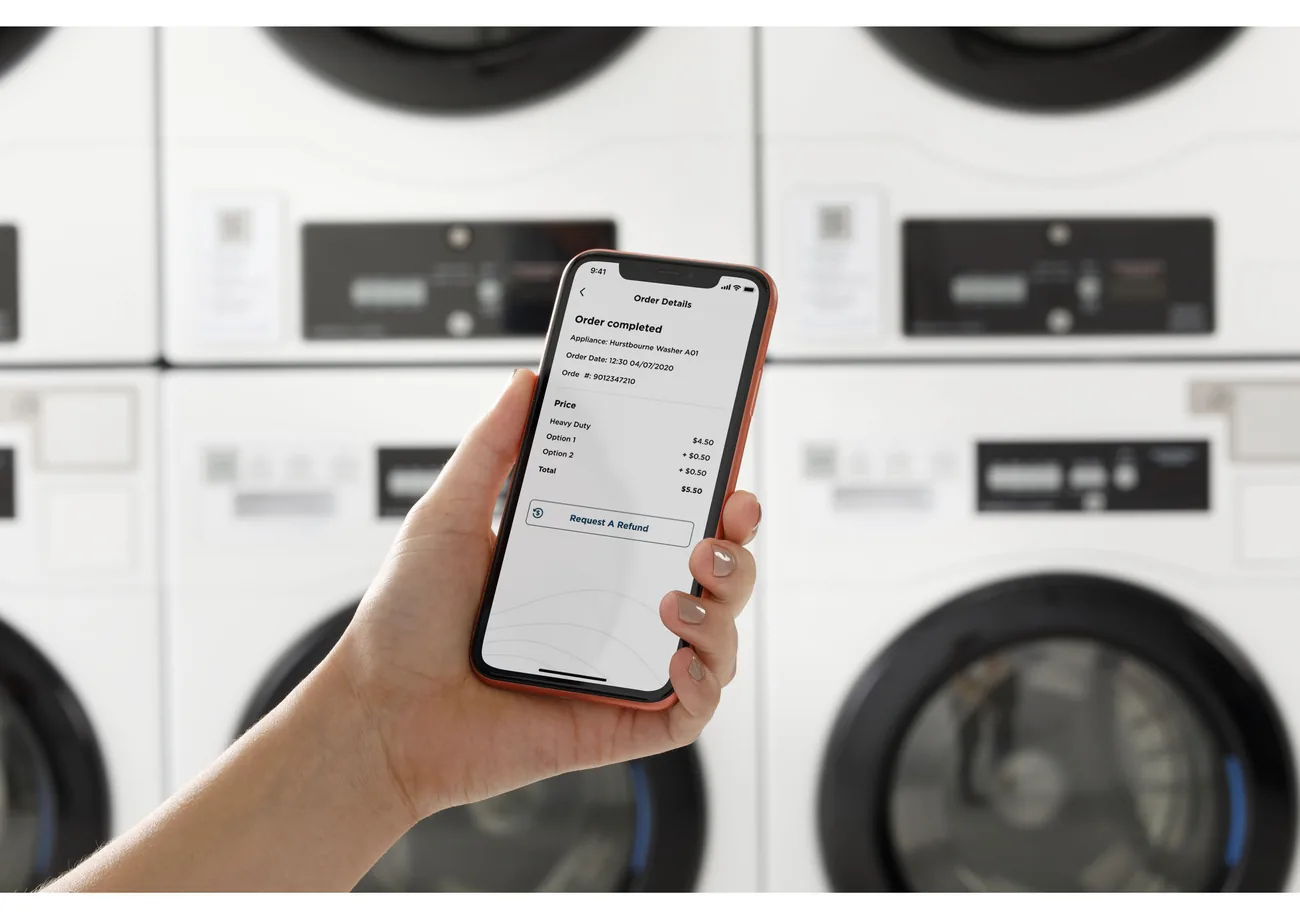 A phone showing a completed laundry order in front of a row of stacked GE machines